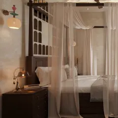 A close-up of the four-poster bed, where sheer curtains create a dreamy, ethereal feel. The traditional wooden headboard with its arched cutouts adds a touch of heritage and craftsmanship.
