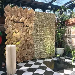 A highly modern and artistic backdrop. This piece combines a wall of gold dried palm leaves with a textured gold sequin panel for a unique and glamorous photo opportunity.