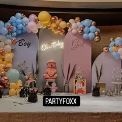 A "Boy or Girl" gender reveal party setup with pink and blue arched backdrops, a central "Oh Baby" neon sign, and a teddy bear prop.