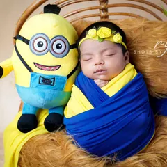 One in a minion. This adorable newborn is wrapped in yellow and blue, sleeping soundly next to his favorite cartoon character during a themed shoot at home.