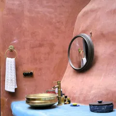 We love using natural, breathable materials like this mud and lime plaster. It not only gives the wall a beautiful, earthy texture but also helps regulate the temperature, keeping the home cool naturally. The brass sink and blue countertop add a touch of modern craft.