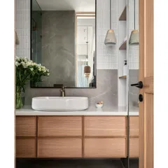 In this master bathroom, a modern aesthetic unfolds through grey matte stone finish tiles and white kitkat tiles. The design highlights a striking white composite marble counter and a mirror framed in black metal.