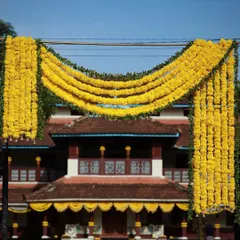 A grand floral arch made of marigolds frames the entrance to a traditional Kerala home, creating a warm and festive welcome for wedding guests.