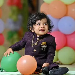 A candid portrait of a young boy with curly hair, smiling as he plays with balloons at his party. We aim to capture these natural, happy expressions that show a child's true personality.