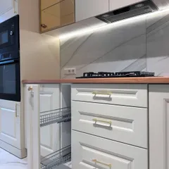 This view highlights the practical storage solutions within our classic kitchen designs, such as this pull-out wire basket drawer, perfect for organizing bottles and jars.