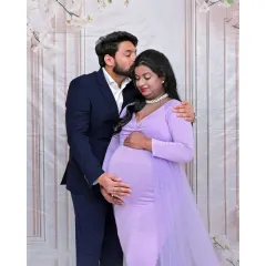 A tender moment between a couple. The father-to-be gently kisses his partner's forehead, a simple gesture of love and support. The coordinated lavender and navy outfits look sharp against the clean backdrop.