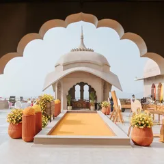 The entrance to the 'Jaipur Wali Haldi', framed by a traditional Rajasthani arch. The path is lined with marigold flowers, setting a festive and welcoming tone for the Mela-themed celebration.