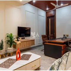 This angle highlights the room's multi-functionality, with a comfortable lounge area and a wall-mounted television for breaks or informal presentations. The space is designed to be both a productive office and a relaxing retreat.