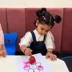 A young artist uses a sponge dabber to color a flower. This activity not only unleashes creativity but also strengthens the small muscles in her hands, preparing her for writing.