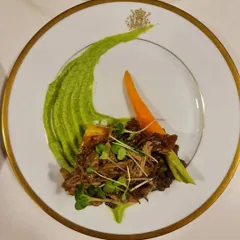 A plated dish of slow-cooked lamb on a smear of green pea puree. This is the kind of refined, flavorful course you can expect from our curated sit-down dinner menus.
