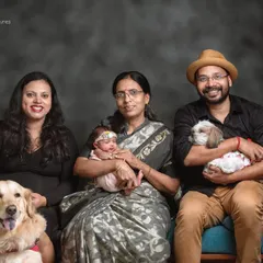 The whole family is here. This portrait includes the new parents, a proud grandmother holding the newborn, and their two beloved dogs, a Golden Retriever and a Shih Tzu.