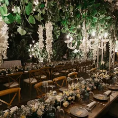 A close-up of the tablescape from a beautiful wedding dinner. The setting features elegant chandeliers dripping with white wisteria, creating a magical, intimate atmosphere for guests.