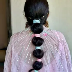 A playful and chic bubble braid for a Mehendi look. I used pastel-colored threads to wrap sections of the braid, adding a fun and unique detail that ties into her colorful outfit.