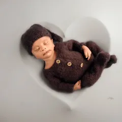 A minimalist and modern newborn portrait of a baby in a brown knit outfit, sleeping inside a heart-shaped white bowl.