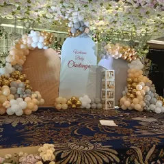 For grand celebrations in large halls, I design elaborate stage setups like this one for baby Chaitanya's welcome party. This features multiple backdrops, large organic balloon arches in gold, white, and beige, and transparent 'PARTY' boxes, all under a stunning floral ceiling.