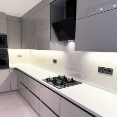 This close-up highlights the seamless integration of a four-burner hob and a sleek black chimney into the modern cabinetry. The handle-less drawers and high-gloss finish are hallmarks of our contemporary kitchen designs.