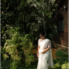 A beautiful black and white portrait of the bride in her white saree, walking through a lush garden. The natural setting and her graceful posture create a timeless image.