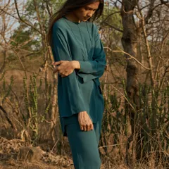 A fashion portrait set in a dry, wooded landscape. The deep teal of the outfit stands out beautifully against the natural, earthy tones of the environment.