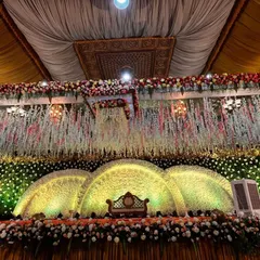 A classic reception stage with a massive, arched floral backdrop. The warm lighting highlights the thousands of flowers used, creating a rich and opulent atmosphere for a truly grand wedding.
