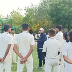 A group of attentive trainees listens as Virender Sehwag shares his expertise during an outdoor masterclass. We foster an environment of focused learning and open interaction.