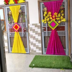 For pre-wedding functions at home, I create vibrant and traditional decor. Here, I've decorated two entrances for a Haldi or Mehendi ceremony using bright yellow and magenta drapes, complemented by traditional hangings and floral elements.
