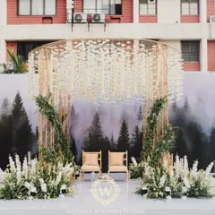 A modern minimalist mandap that perfectly blends nature and contemporary design. The structure features a backdrop of a misty forest, a canopy of hanging white florals, and lush green arrangements.