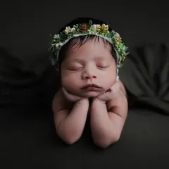 A dramatic version of the 'chin on hands' pose against a dark, moody background, which makes the baby's features stand out.
