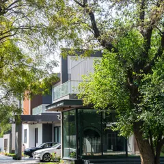 At Triveni Farmhouse, the architecture is nestled among mature trees. The home's modern design, with its glass-wrapped corner and cantilevered balconies, creates a beautiful contrast with the organic forms of the surrounding nature.