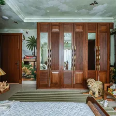 This view showcases the custom wooden wardrobes with mirrored panels, which reflect the beautiful jungle mural on the opposite wall. Every element, including the stuffed lion, adds to the room's playful explorer theme.