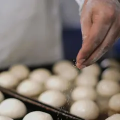 The baker's touch. A chef sprinkles sesame seeds onto fresh dough balls before they go into the oven, a simple step that adds so much to the final product.