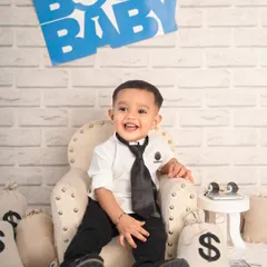 This little boss baby is ready to take over. Dressed in a tiny suit and tie, he's all smiles in his special first birthday setup, complete with money bags and a corner office vibe.