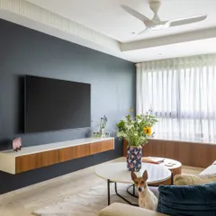 The living room is designed for comfort and style. A dark feature wall anchors the space, while the light-colored sofa, sheer curtains, and the owner's adorable dog add warmth and personality.