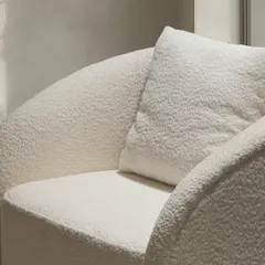 A detailed view of the barrel-back armchair, focusing on the rich, looped texture of the bouclé fabric. This material choice was intentional, designed to soften the chair's simple, geometric form and add a layer of tactile warmth.