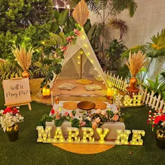 A charming and personal proposal setup in my garden. This bohemian-style arrangement includes a decorated teepee, low picnic seating, and light-up "Marry Me" letters for a sweet and memorable moment.