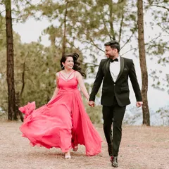 A joyful, candid shot of a couple running hand-in-hand through a forest clearing, her vibrant pink dress flowing behind her, capturing pure happiness and movement.