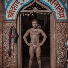 A wrestler stands proudly at the entrance of the Shri Shahu Vijayi Gangavesh Taleem, his body covered in the training mud. This powerful stance captures the pride and dedication of a Kolhapuri Pailwan.