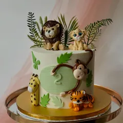 A safari cake for a second birthday, complete with a swinging monkey. This design features a lion, lion cub, tiger, and giraffe, all set against a backdrop of fondant jungle leaves.
