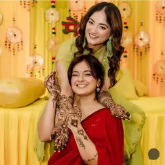 A beautiful moment between friends or sisters at a mehandi function, both showing off their unique henna designs.