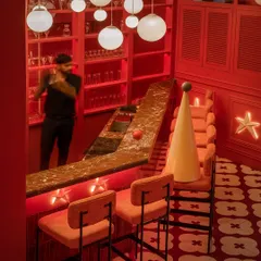 The bar at Masala is drenched in a dramatic red glow, with a cascade of moon-like pendants creating a celestial feel. The design is theatrical and immersive, intended to make the simple act of ordering a drink feel like part of an event.