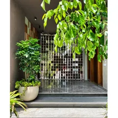 The entrance to the House of Terraces is framed by lush greenery and a sculpted metal screen. This landscape gesture sets the rhythm for arrival, creating a private foyer that quietly unfolds as you approach the home.