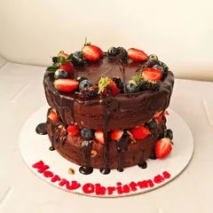 A festive two-tiered chocolate cake for a Christmas celebration. This naked cake is layered with chocolate ganache and generously topped with fresh strawberries, blueberries, and mulberries.