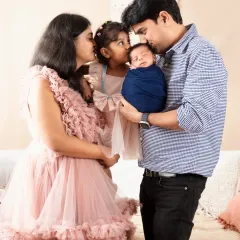 A heartwarming family portrait capturing a tender moment. The mother, father, and older sister share kisses with the newest family member, a newborn boy wrapped snugly in blue.