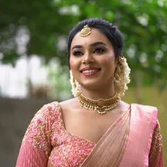 A beautiful and happy bride with her hair styled in a classic updo. The jasmine flowers tucked into the side of the bun add a traditional touch that complements her soft pink saree.