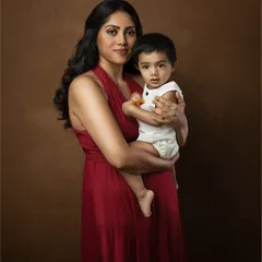 A close-up fine art portrait of a mother holding her child. The warm brown backdrop and her direct gaze create a powerful and soulful image.