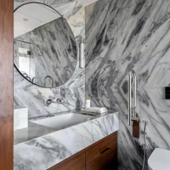 This bathroom in the Parishram residence features a different kind of marble, with bold, sweeping grey veins. A large, circular mirror and clean, modern fixtures complete the elegant design.