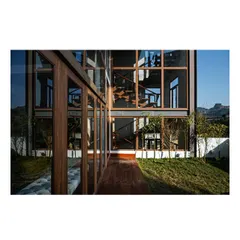 The exterior facade showcases the home's modern aesthetic, with clean lines and large glass panels. The reflection in the glass creates a beautiful symmetry with the surrounding greenery and the building's structure.