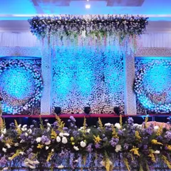 A modern reception stage featuring circular floral wreaths against a backdrop of white flowers and dramatic blue lighting, offering a contemporary yet elegant look.