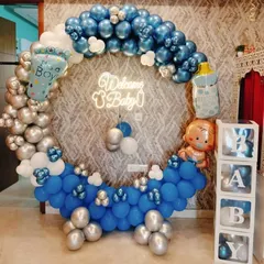 A grand welcome for a baby boy with a full circular balloon ring. The blue, silver, and white balloons are complemented by a "Welcome Baby" neon sign and transparent "BABY" boxes.