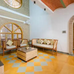 The double-height living area uses a combination of Jaisalmer yellow and grey Kota stone for the flooring. Large arched windows and exposed earth block walls bring in ample daylight and a sense of warmth.