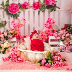 Dressed in a vibrant red wrap and matching headband, a newborn slumbers in a basket surrounded by an explosion of pink and red flowers. This demonstrates our use of bold, coordinated colors to create visually stunning and artistic photographs.